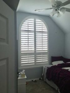 bed in room with wood plantation shutters window